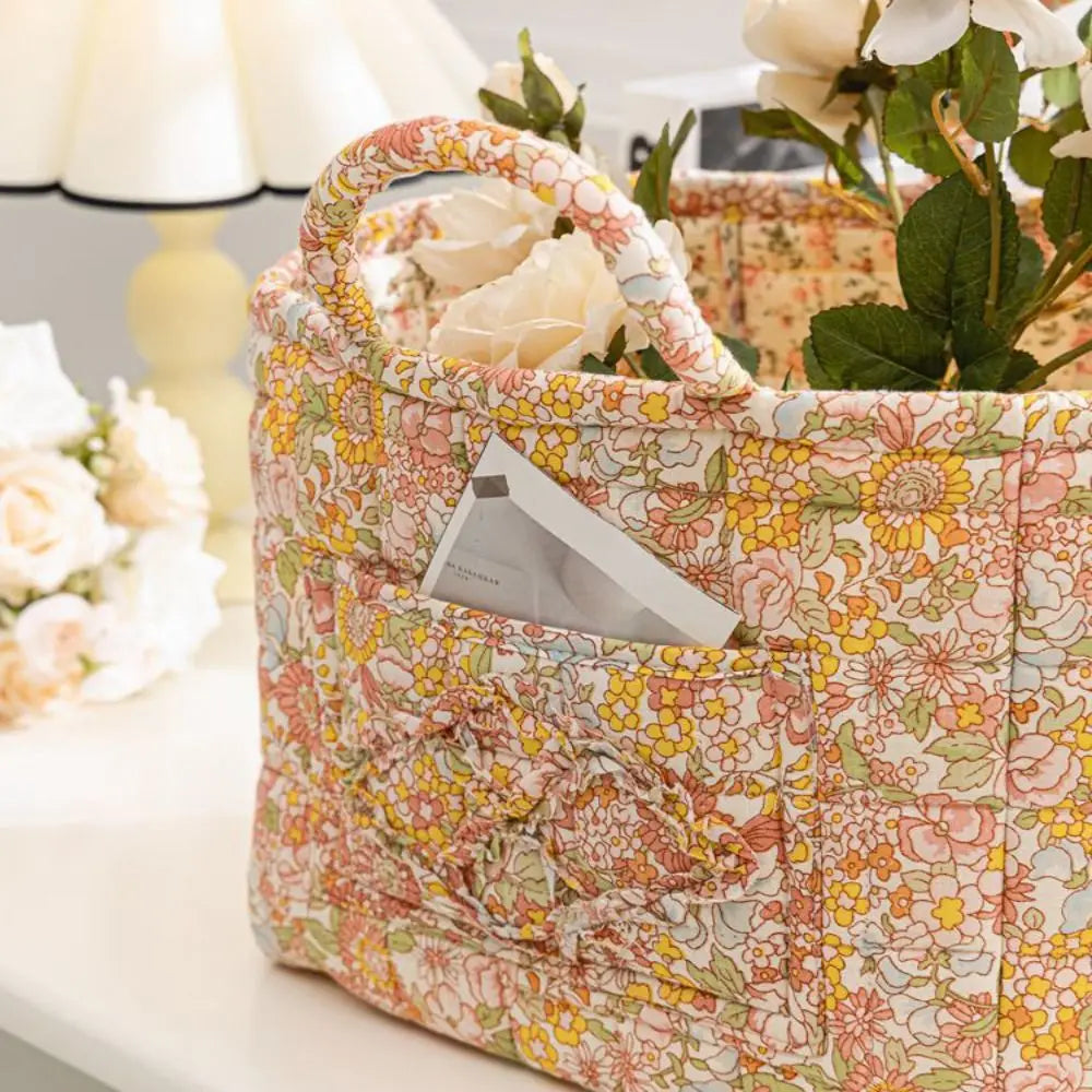 A quilted fabric storage basket with light floral pattern and carry handles sits on a white surface.