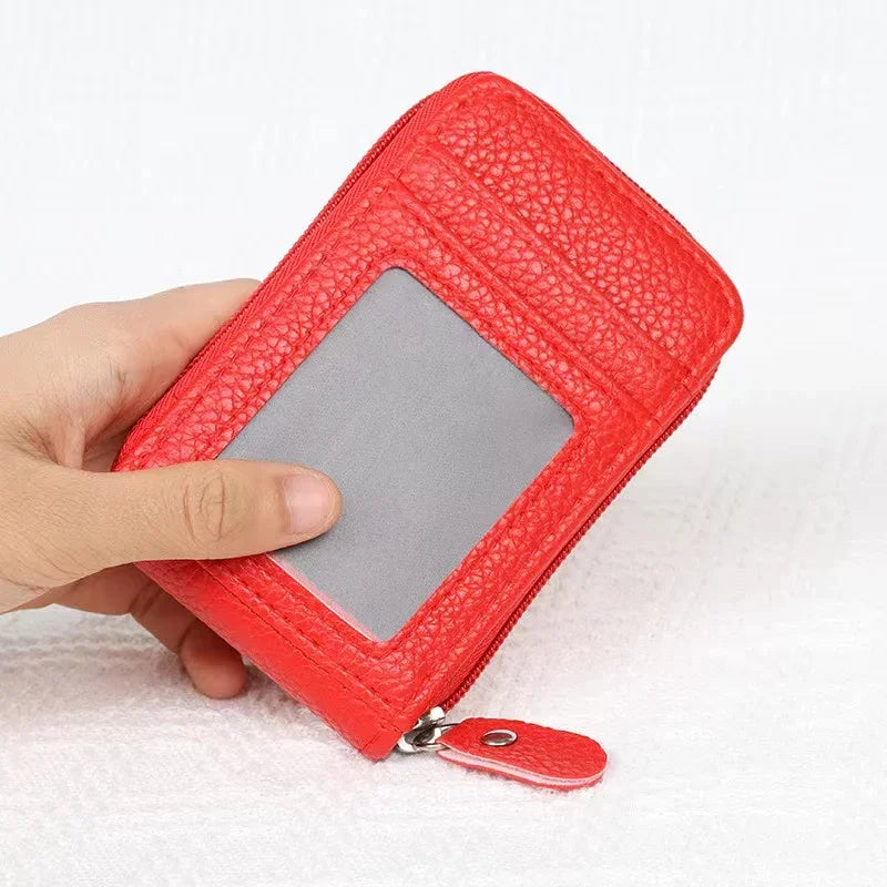A hand holds a red textured card holder wallet with a clear plastic slot and a silver zipper pull.