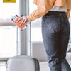 A person holds an orange RFID blocking passport wallet in their hand next to a silver rolling suitcase.