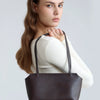 A woman models a dark brown genuine leather mini shoulder bag with adjustable straps.