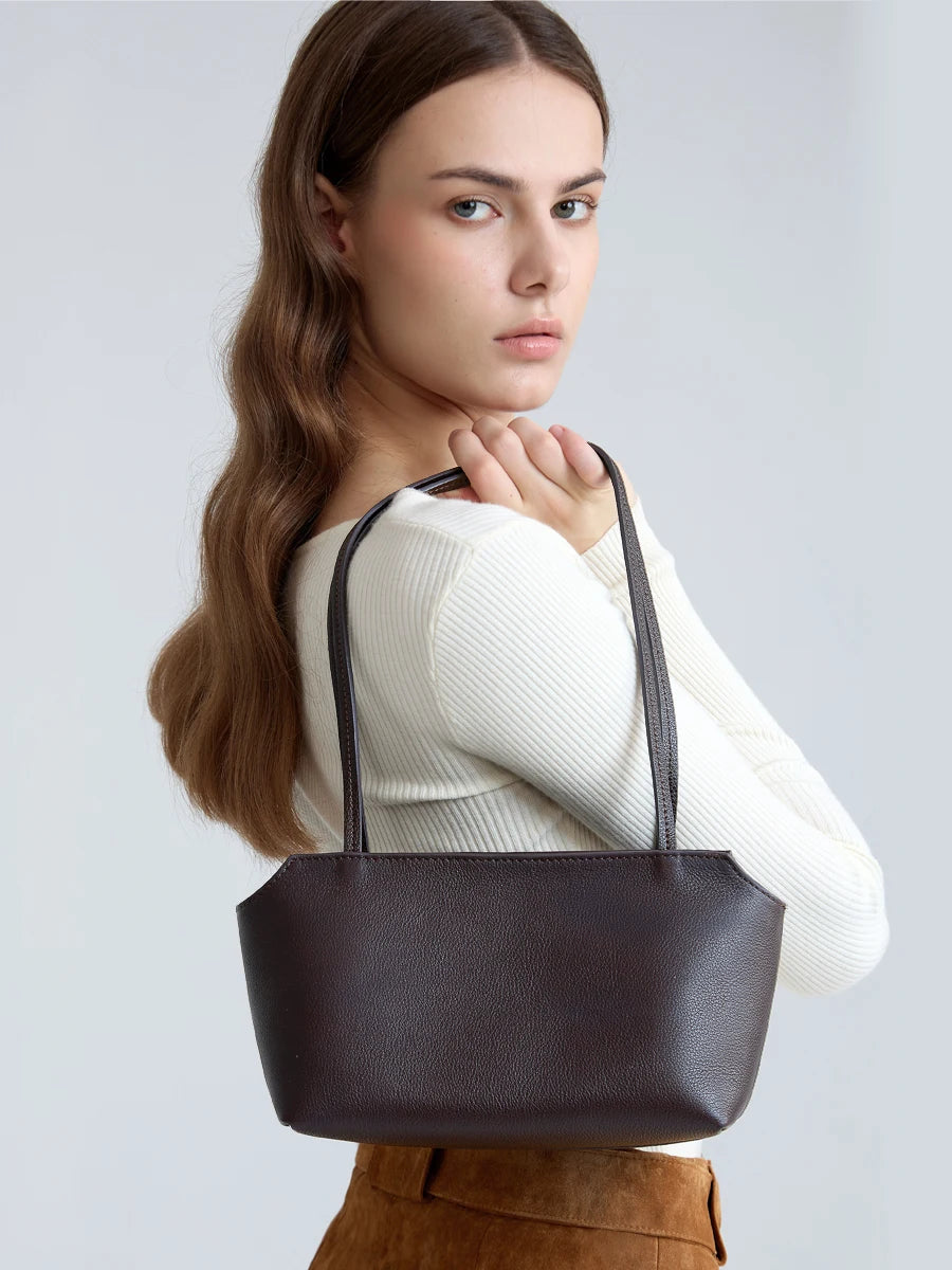 A woman models a dark brown genuine leather mini shoulder bag with adjustable straps.