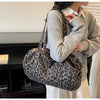 A woman holds a leopard print canvas tote bag with an adjustable shoulder strap against a light background.