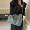 A woman holds a light blue nylon tote bag with brown leather straps against a light wall.