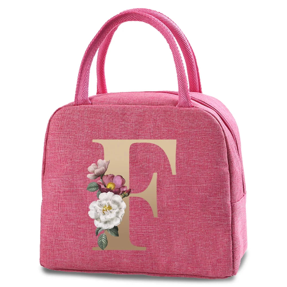 A pink insulated canvas lunch bag featuring a large gold letter F and a small floral design.