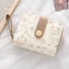 A beige cat cartoon coin purse and card holder wallet with a leather strap resting on a white fabric background.