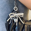A black faux leather bag with a pearl bowknot keychain hanging from a silver chain.