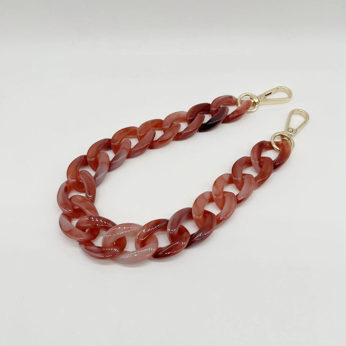 A close-up of a reddish-brown acrylic chain bracelet with gold-colored clasps.