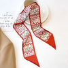 Foulard pour cheveux floral en soie plié avec motifs géométriques rouges et blancs à côté d'une note manuscrite.