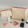 A cream quilted makeup bag with red trim and a heart pattern, next to a pink heart and a small black item.