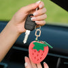 A hand holds a strawberry-shaped coin purse keychain with a silver key attached.