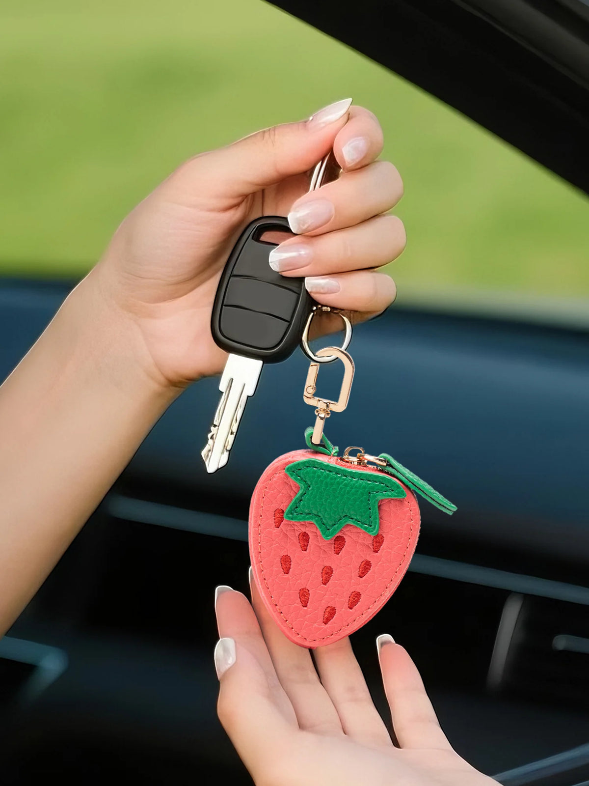 A hand holds a strawberry-shaped coin purse keychain with a silver key attached.