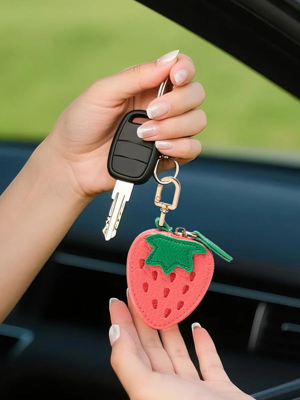 A hand holds a strawberry-shaped coin purse keychain with a silver key attached.