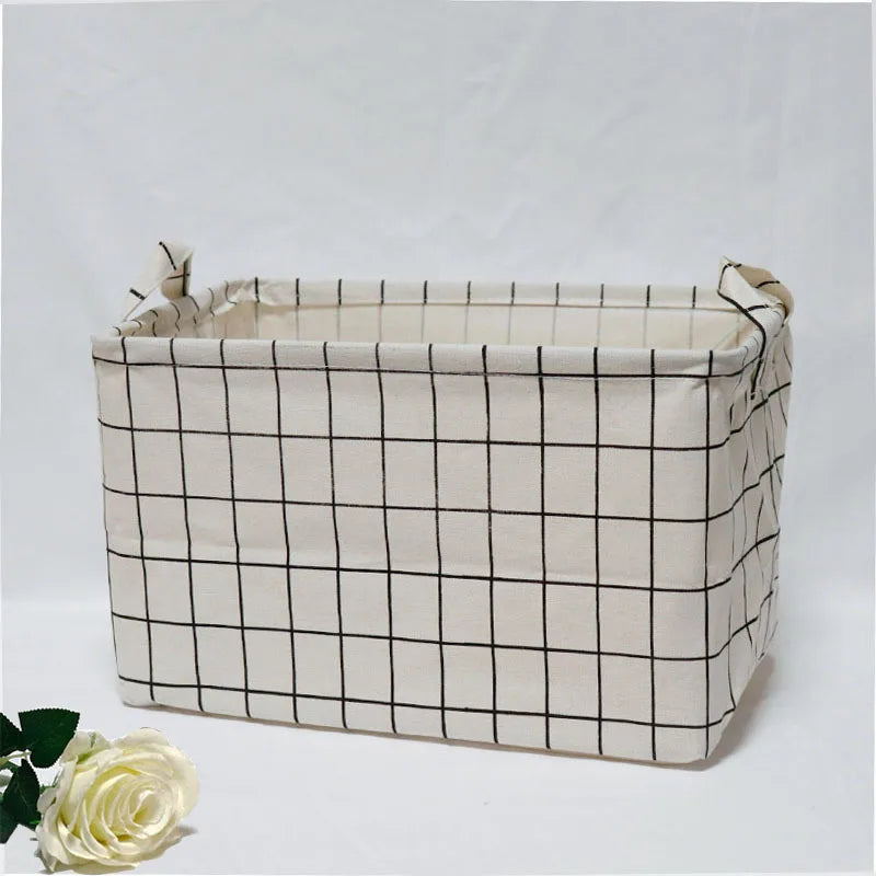 A rectangular beige fabric storage basket with a black grid pattern and handles, shown against a white background.