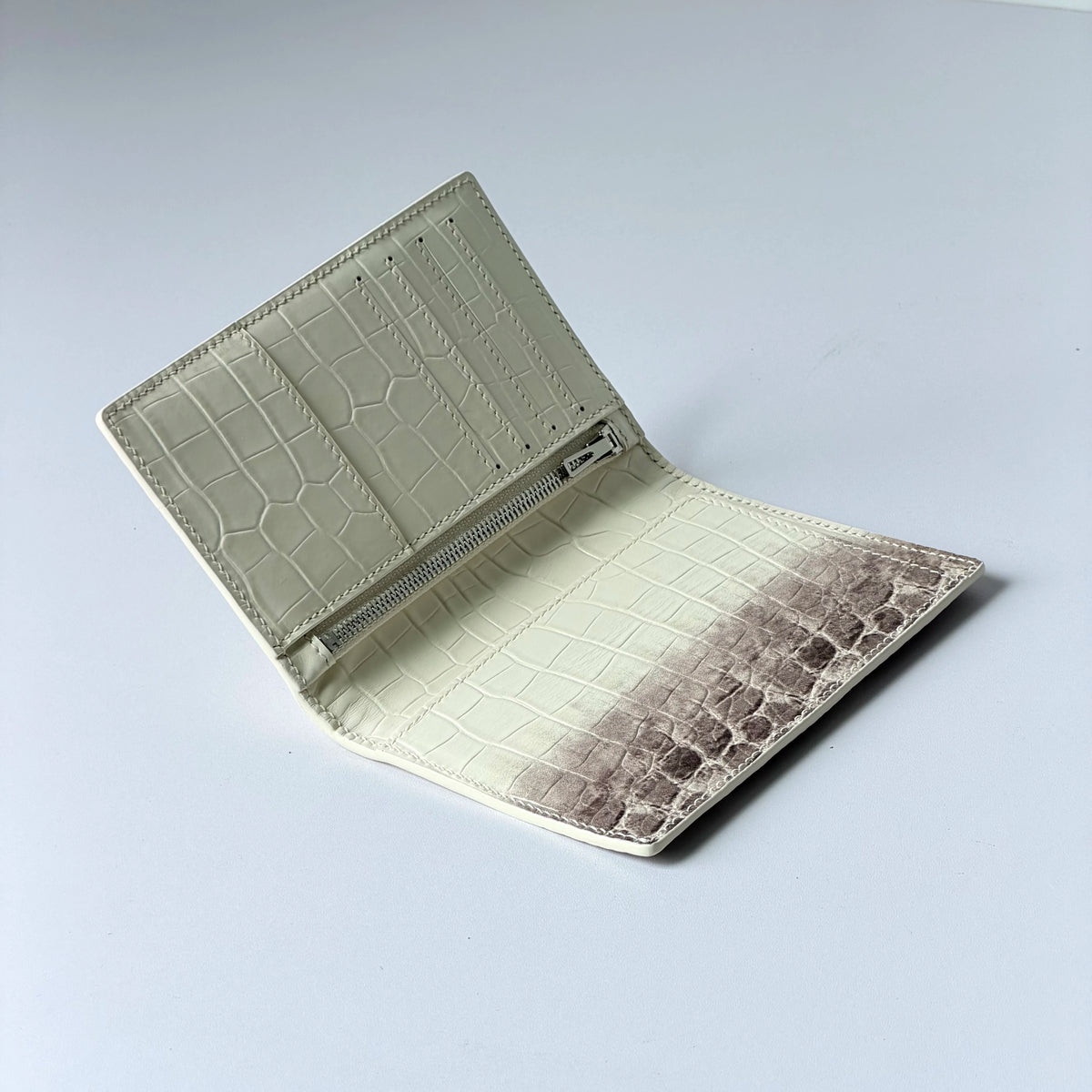 A light cream leather passport holder with a crocodile pattern and custom initials, shown open.