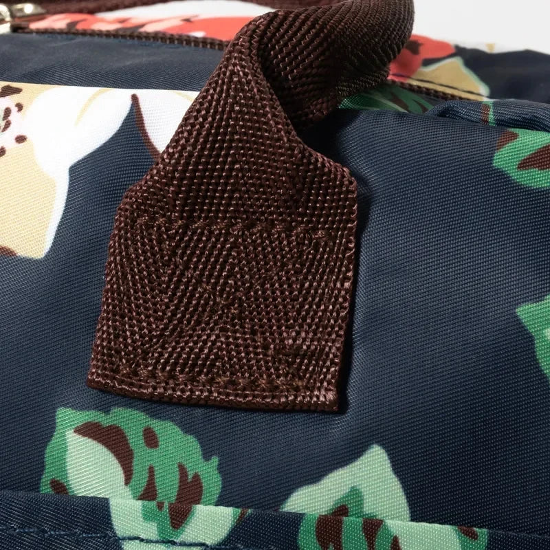 Primer plano de una bolsa de almuerzo de tela oxford azul marino con un lazo de tela marrón y exterior estampado verde y blan