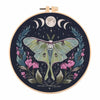 A circular embroidery kit featuring a butterfly design surrounded by floral elements and a moon in a dark background.