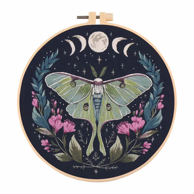 A circular embroidery kit featuring a butterfly design surrounded by floral elements and a moon in a dark background.