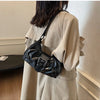 Nahaufnahme einer schwarzen Leder-Schultertasche mit Plissee, getragen von einer Person in einem beigen Oversize-Shirt.