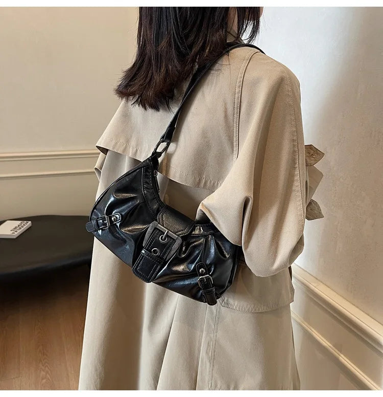 Nahaufnahme einer schwarzen Leder-Schultertasche mit Plissee, getragen von einer Person in einem beigen Oversize-Shirt.