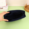 A hand is opening a dark navy felt cosmetic bag insert organizer on a light green surface.