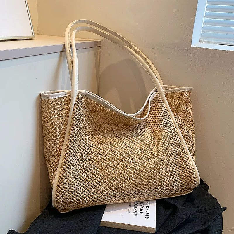 A straw woven tote bag with PU trim and matching pouch resting on a dark cloth.