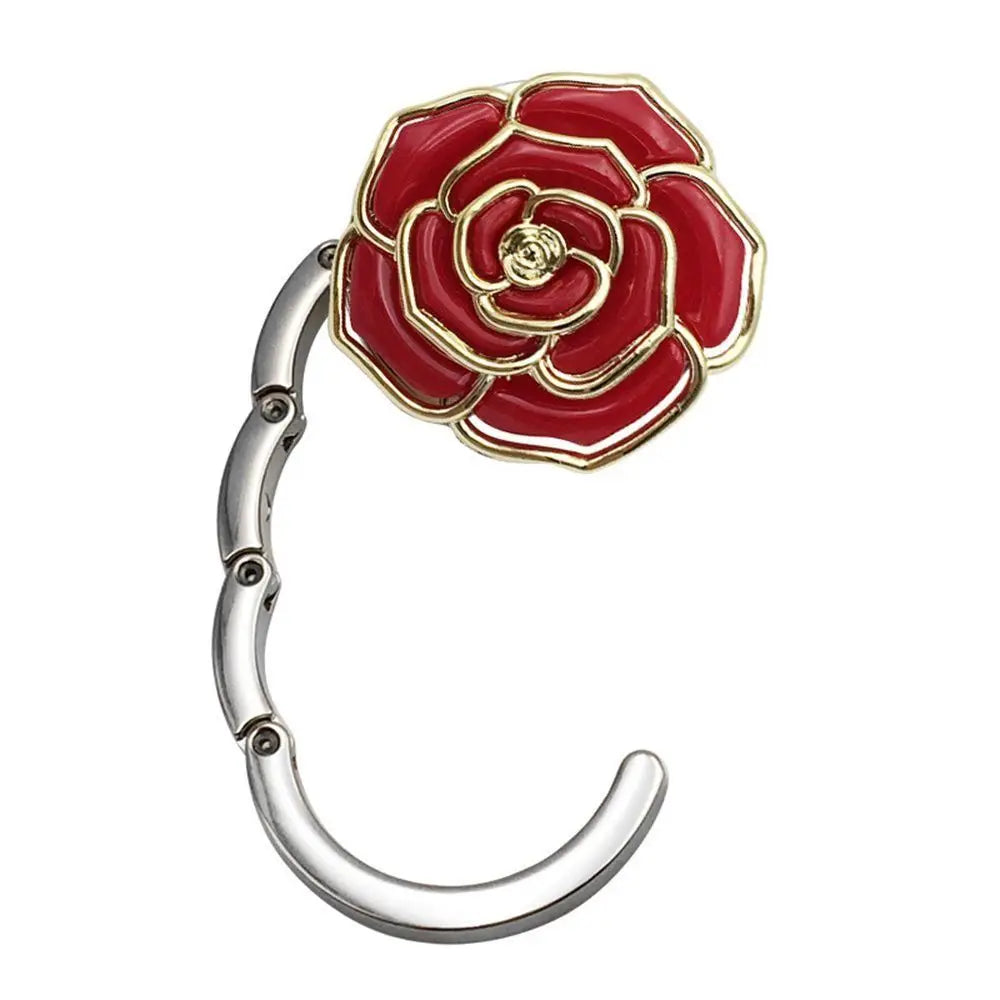 A close-up of a heart-shaped metal foldable bag hook with a red rose design.