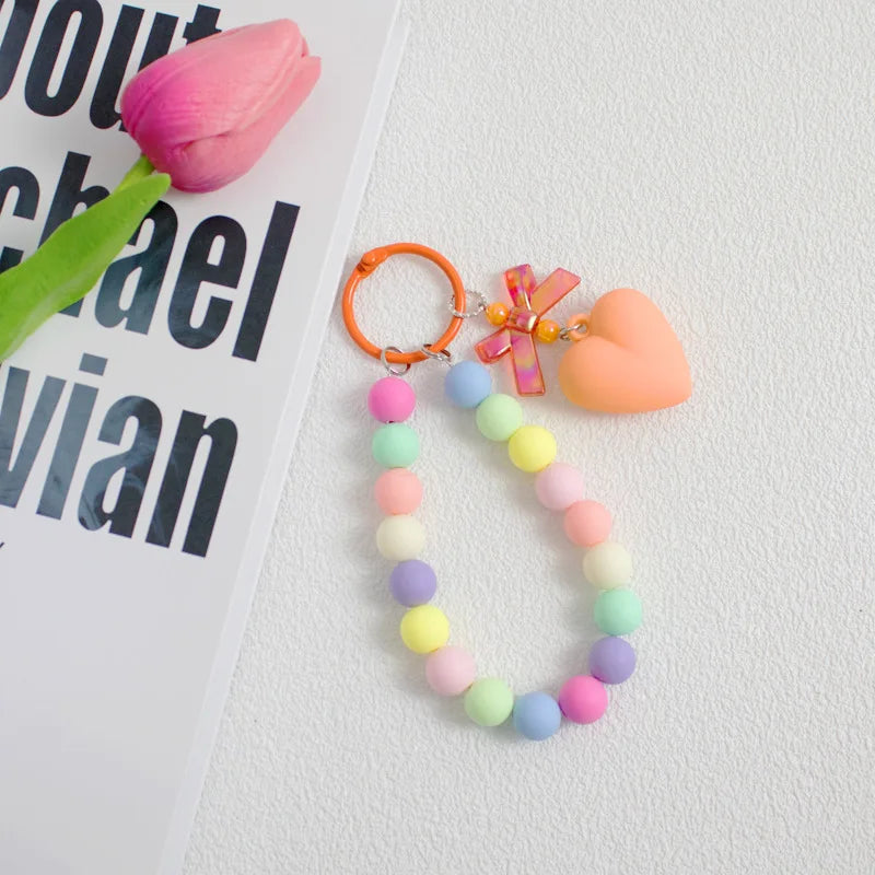 A colorful bead necklace featuring pink, yellow, and blue beads with a pink bow charm attached to an orange O-ring clip.