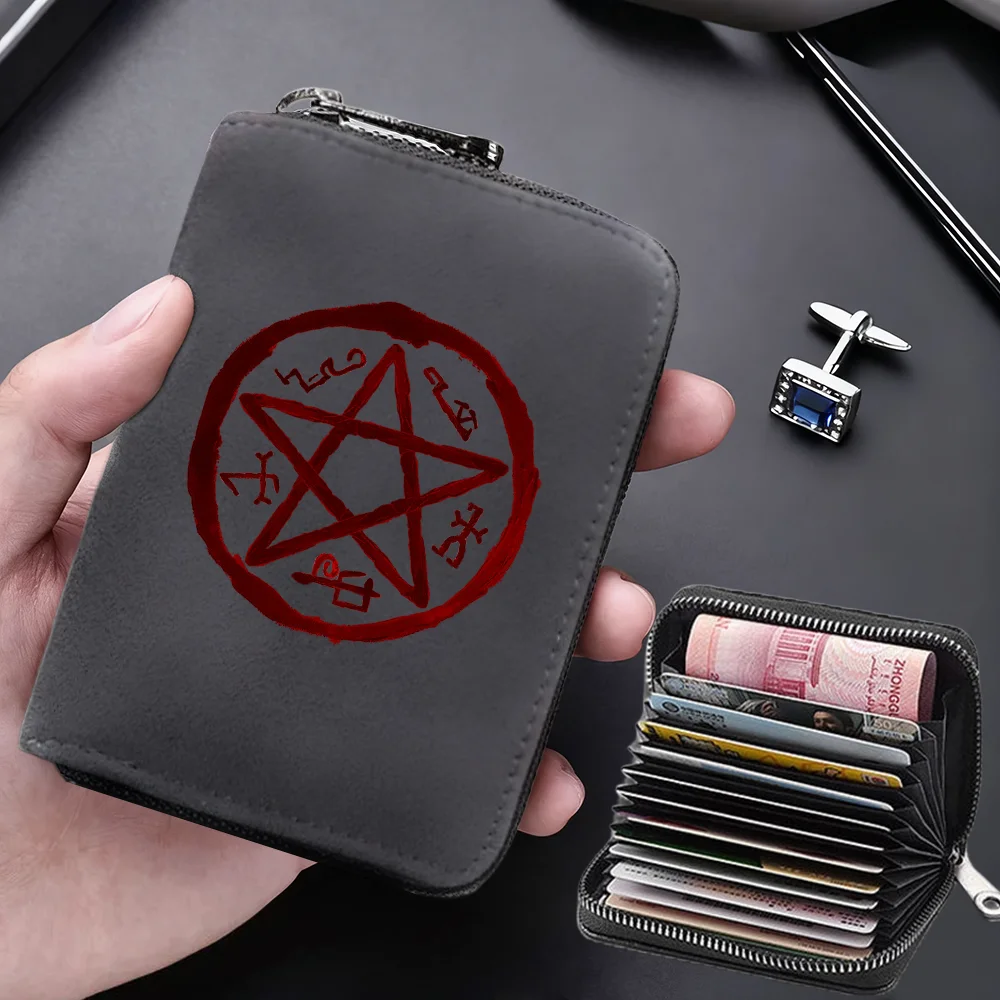 A dark gray compact RFID-blocking card wallet with a red pentagram design is held in a hand next to a stack of credit cards.