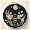 A dark navy embroidery featuring a bee surrounded by green leaves and white flowers with gold accents.