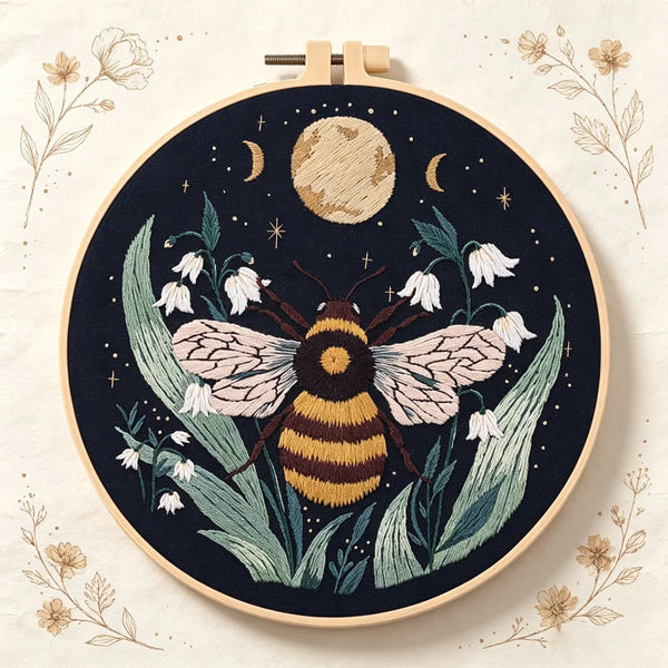 A dark navy embroidery featuring a bee surrounded by green leaves and white flowers with gold accents.