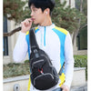 A young man is holding a black nylon chest sling bag while wearing a white long-sleeved shirt outdoors.
