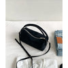 A black faux suede crossbody bag resting on a white surface next to a denim shirt.