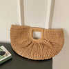 A woven rattan half-moon beach handbag displayed against a white wall.