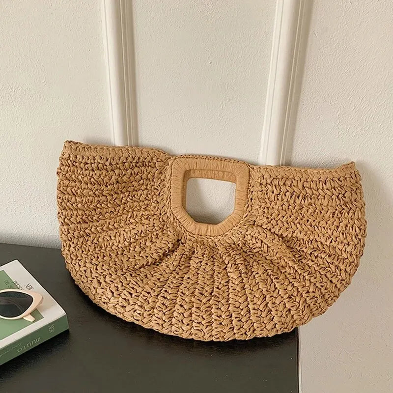 A woven rattan half-moon beach handbag displayed against a white wall.