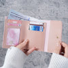 A hand holds a pink card wallet containing cash and credit cards against a gray background.