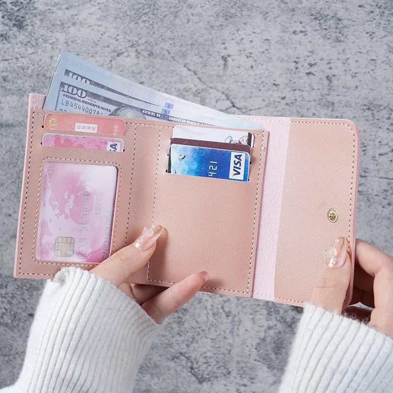 A hand holds a pink card wallet containing cash and credit cards against a gray background.