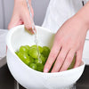 Hands are pouring green grapes into a white plastic drain and storage basket.