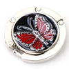 Gancho de mesa plegable de aluminio plateado con diseño de mariposa decorativa.