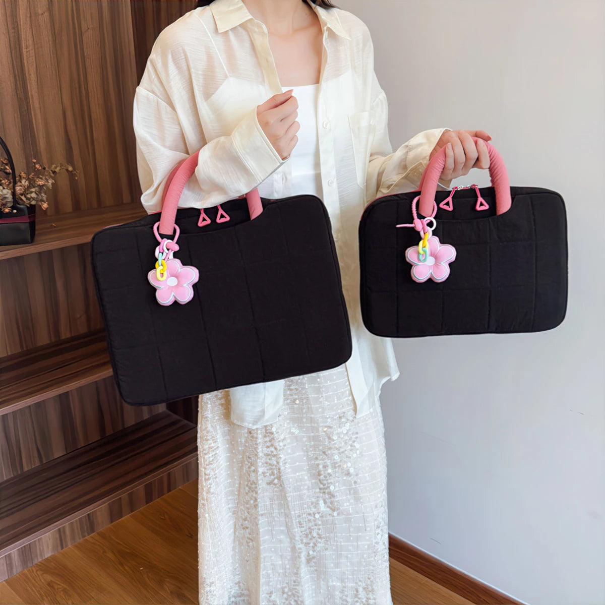 A woman holds a black quilted laptop sleeve with pink handles and a pink flower charm.