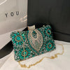 A sparkling emerald green rhinestone evening clutch bag with gold detailing resting on a white surface.
