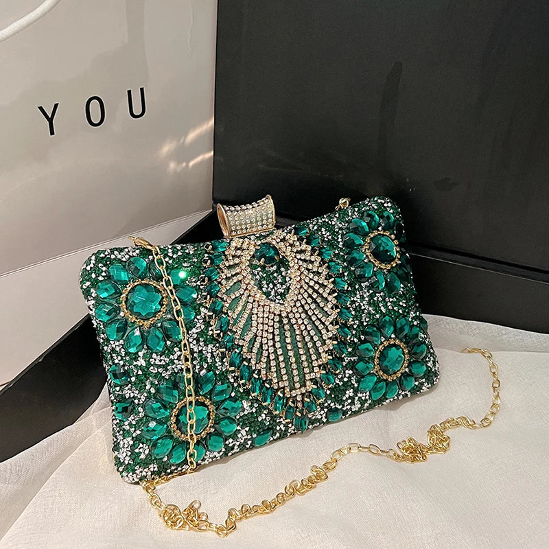 A sparkling emerald green rhinestone evening clutch bag with gold detailing resting on a white surface.