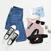 A black multi-functional crossbody storage bag with a zipper pocket and sunglasses displayed next to denim jeans.