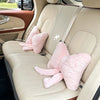 A light beige car seat interior showing a seat with pink fuzzy headrest pillows and lumbar support.