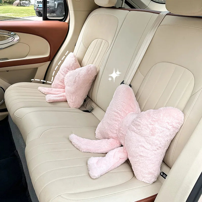A light beige car seat interior showing a seat with pink fuzzy headrest pillows and lumbar support.