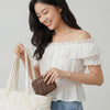 A woman holds a beige canvas tote bag and a brown coin purse against a light gray background.