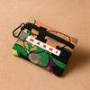 A floral print mini coin purse with a black zipper and carabiner clip resting on a beige surface.