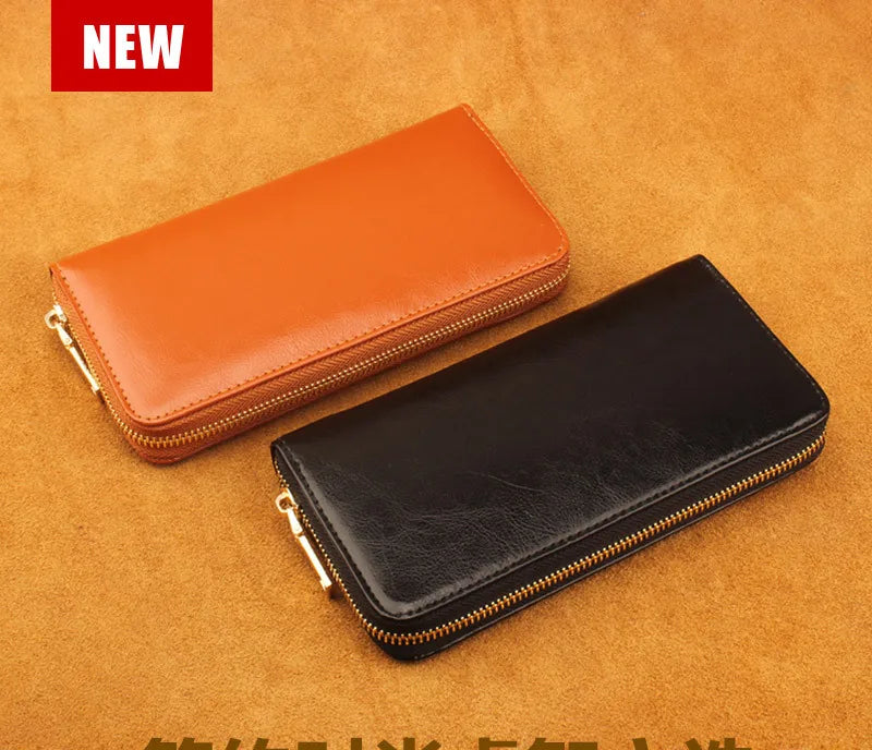 Two genuine leather zipper wallets, one orange and one black, are displayed on a brown textured surface.