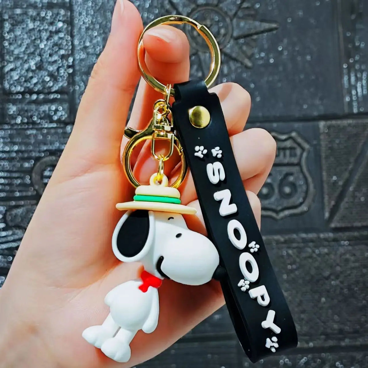 A hand holds a Snoopy 3D silicone keychain set featuring a dog figure and a black tag.