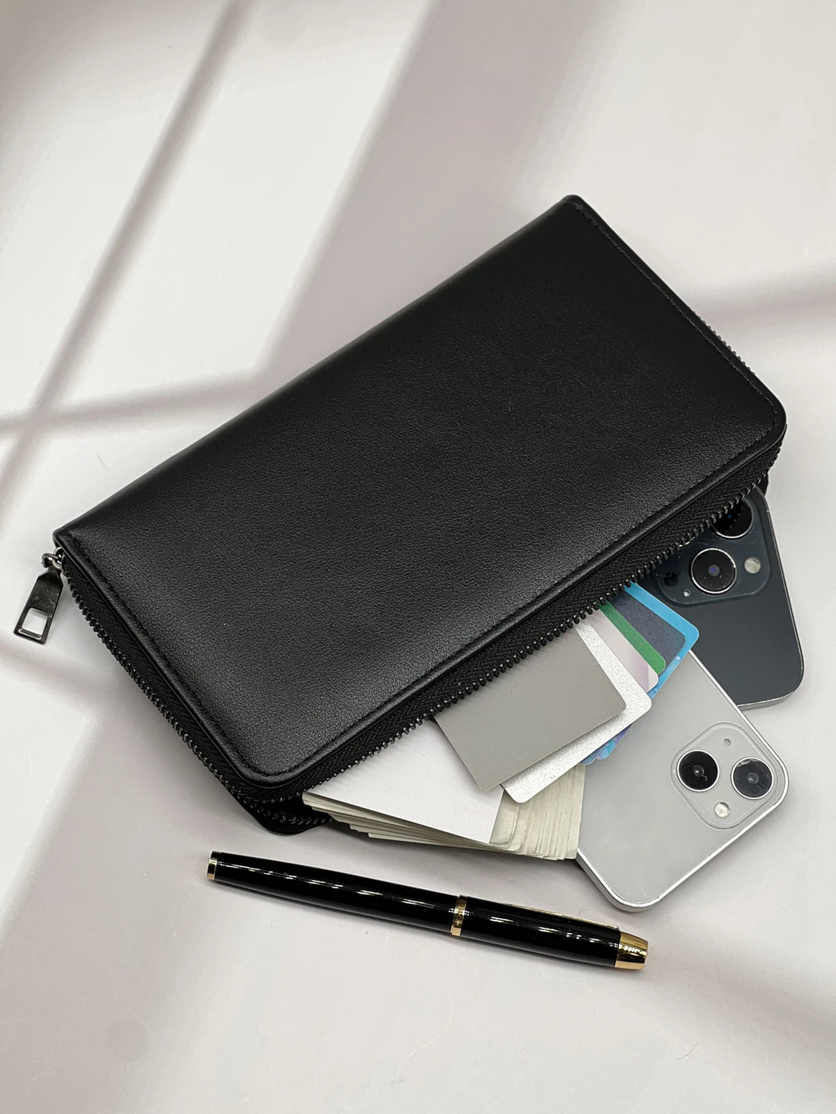 A black multi-card commuter wallet is shown open, displaying various cards and a black pen on a white surface.