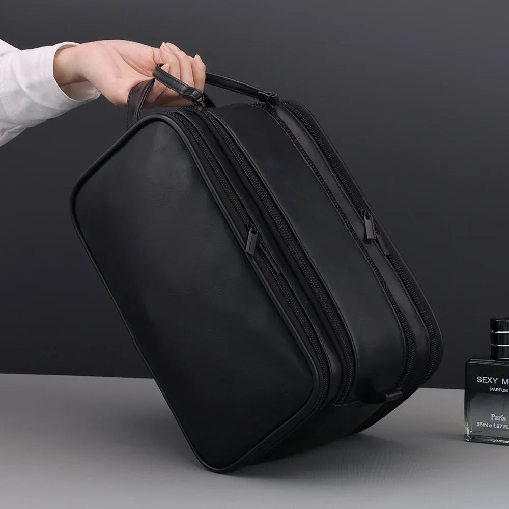 A hand is holding a black PU leather travel toiletry bag with organizer pockets.
